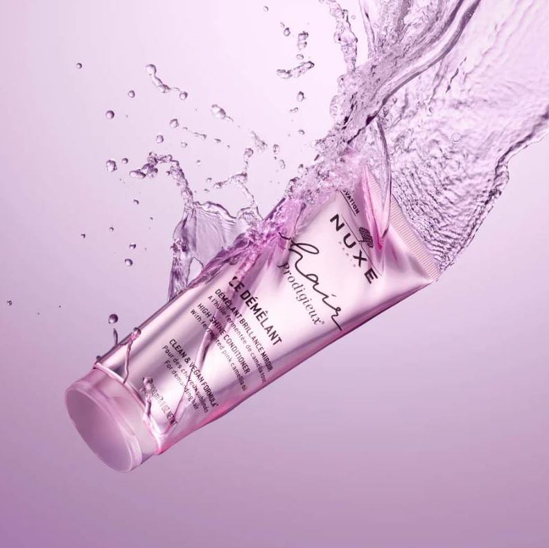 Nuxe hair care product with water splash on a purple background