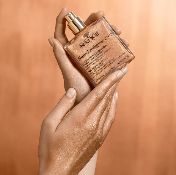 Hand holding a Nuxe skincare product against a warm brown background