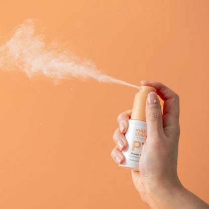 Hand holding a spray bottle with powder against an orange background