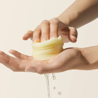 Hand holding a bar of soap with water dripping from it against a beige background