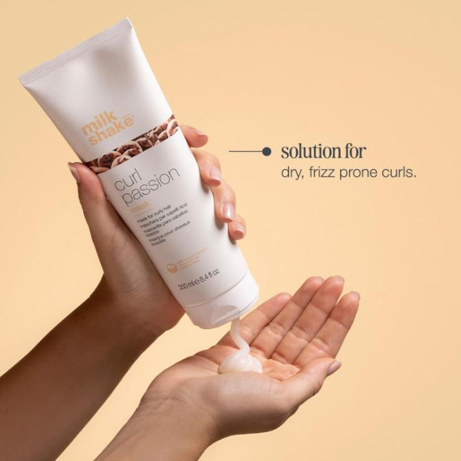 Hand holding a tube of 'milk shake curl passion' product with a beige background