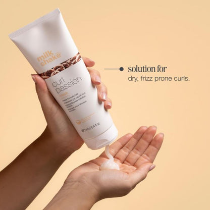 Hand holding a tube of 'milk shake curl passion' product with a beige background