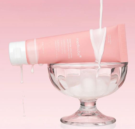 Pink skincare product being poured into a glass bowl against a pink background