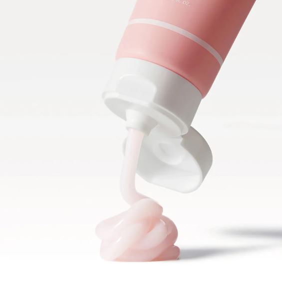 Pink and white cosmetic tube with cream being squeezed out on a light gray background