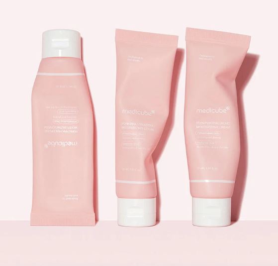 Three pink skincare products with white caps on a light pink background
