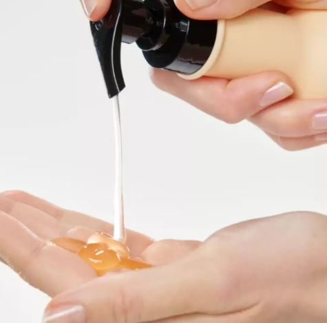 Hand pouring honey from a container onto another hand against a white background