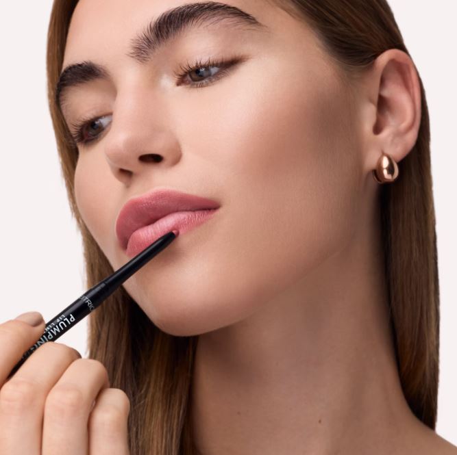 Woman applying lip liner with a pencil on a plain background