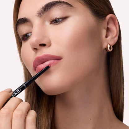 Woman applying lip liner with a pencil on a plain background