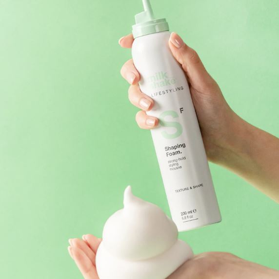 Hand holding a bottle of 'milk made' shaping foam against a green background
