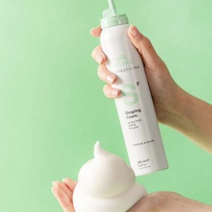 Hand holding a bottle of 'milk made' shaping foam against a green background
