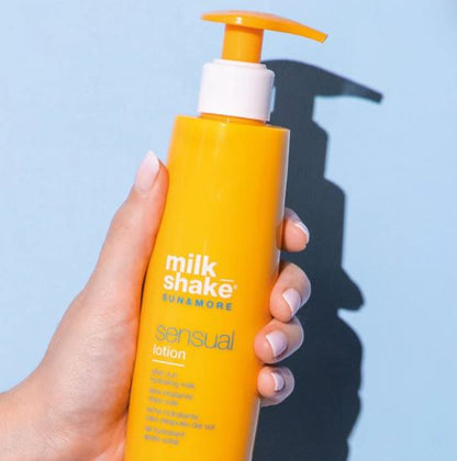 Hand holding a yellow bottle of milkshake sensual lotion against a light blue background