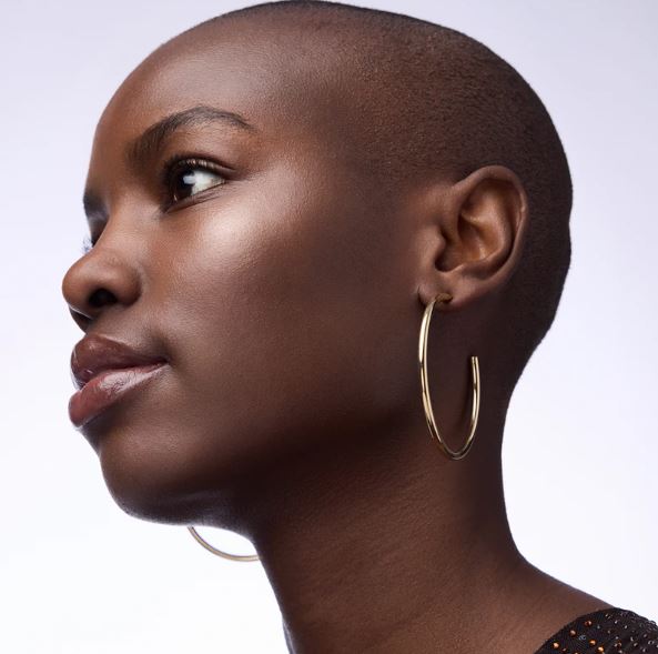 Close-up of a woman wearing gold hoop earrings against a neutral background