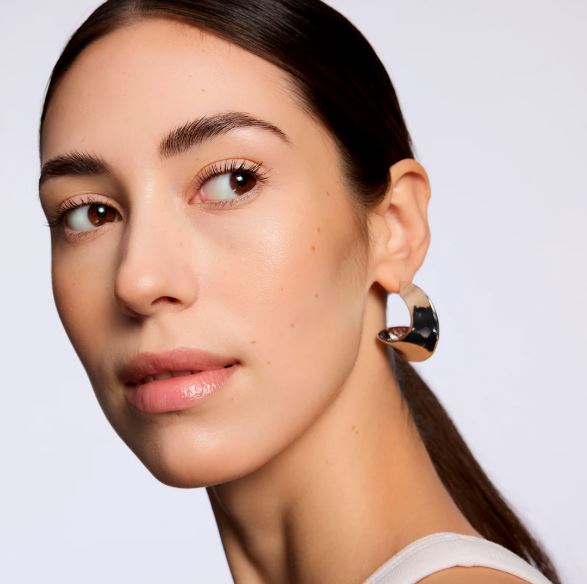 Close-up of a woman wearing a gold earring against a light background