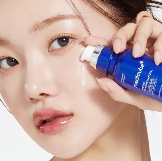 Person applying a blue bottle of Medicube product to their face.