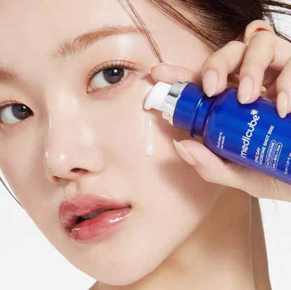 Person applying a blue bottle of Medicube product to their face.
