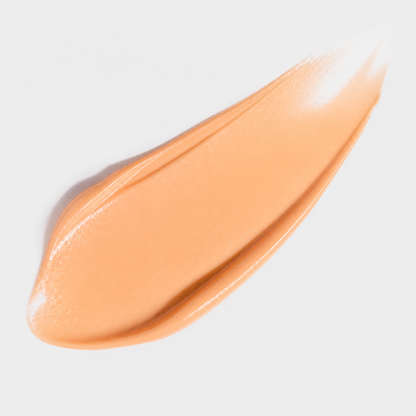 Swatch of peach-colored makeup cream on a light gray background