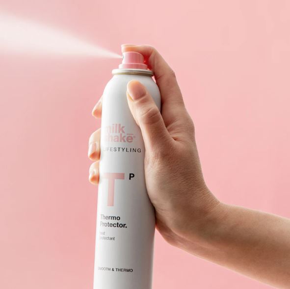 Hand holding a can of Silk & Kale styling product against a pink background