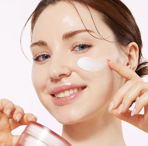 Woman applying cream to her face with a white background