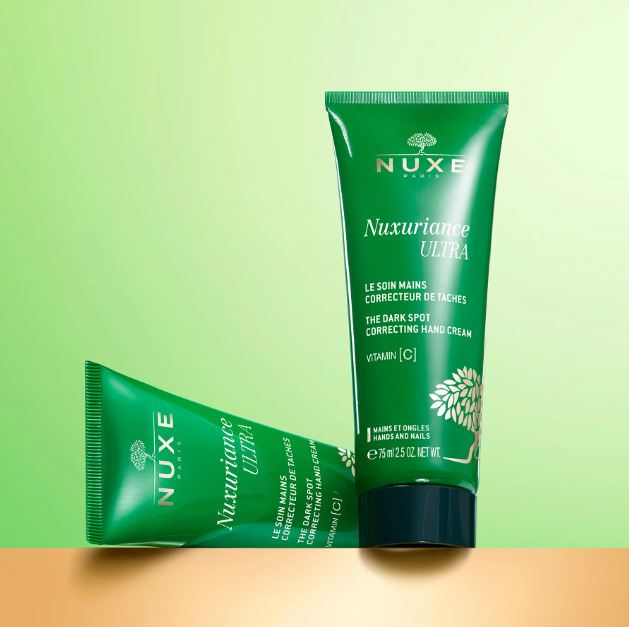 Green Nuxe hand cream tube on a gradient green and orange background