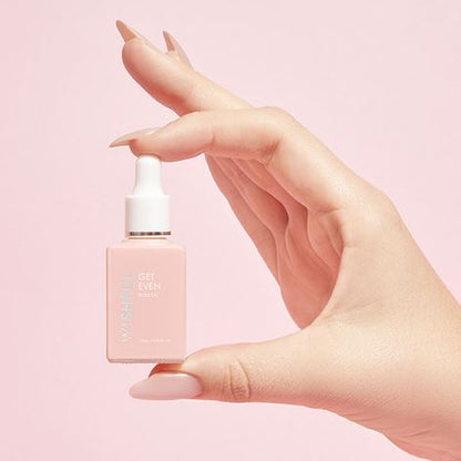 Hand holding a pink skincare serum bottle against a light pink background
