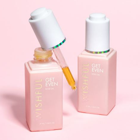 Two pink skincare bottles with droppers on a pink background